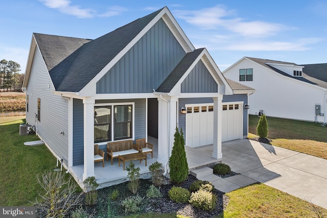 view of front of home with a garage, covered porch, a front yard, and central AC