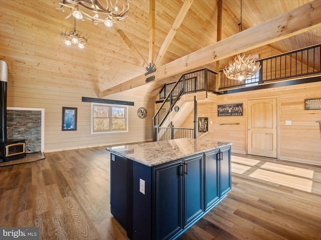 kitchen with wooden walls, a center island, a wood stove, and high vaulted ceiling