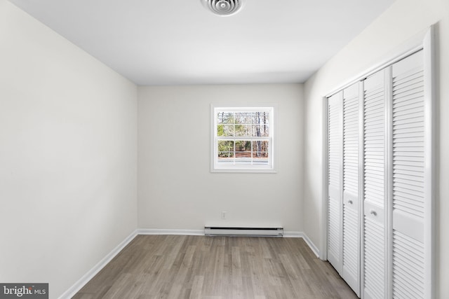 unfurnished bedroom with a closet, light hardwood / wood-style floors, and a baseboard heating unit