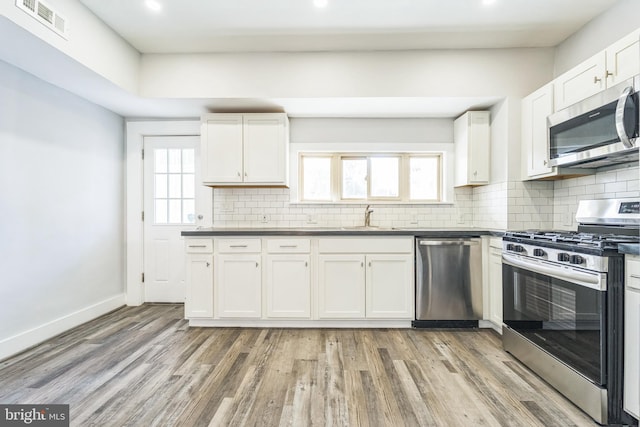 kitchen featuring appliances with stainless steel finishes, light wood-type flooring, backsplash, sink, and white cabinetry