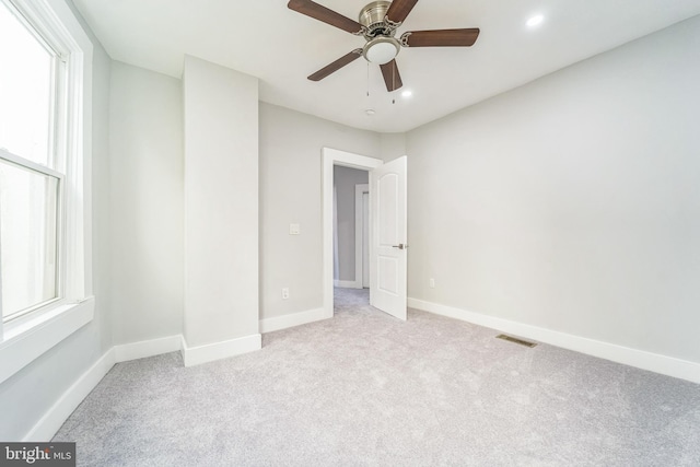 unfurnished room with a wealth of natural light, ceiling fan, and light carpet