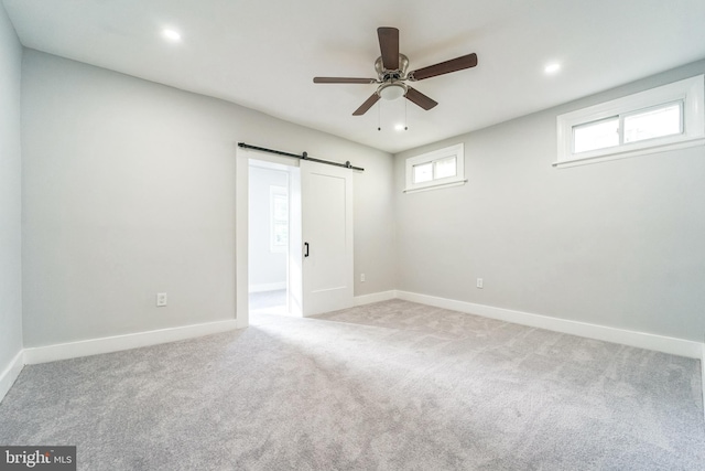 carpeted spare room with plenty of natural light, a barn door, and ceiling fan