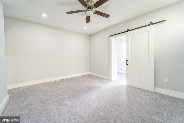 empty room with ceiling fan, a barn door, and light colored carpet