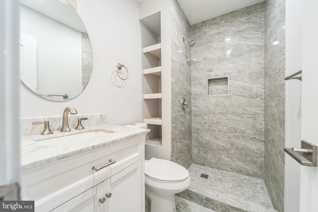 bathroom with toilet, a tile shower, vanity, and built in features