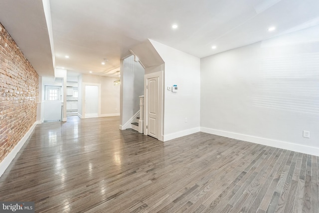 829 Chauncey Ave, Baltimore, MD 21217 - unfurnished living room with wood finished floors, baseboards, brick wall, and stairway