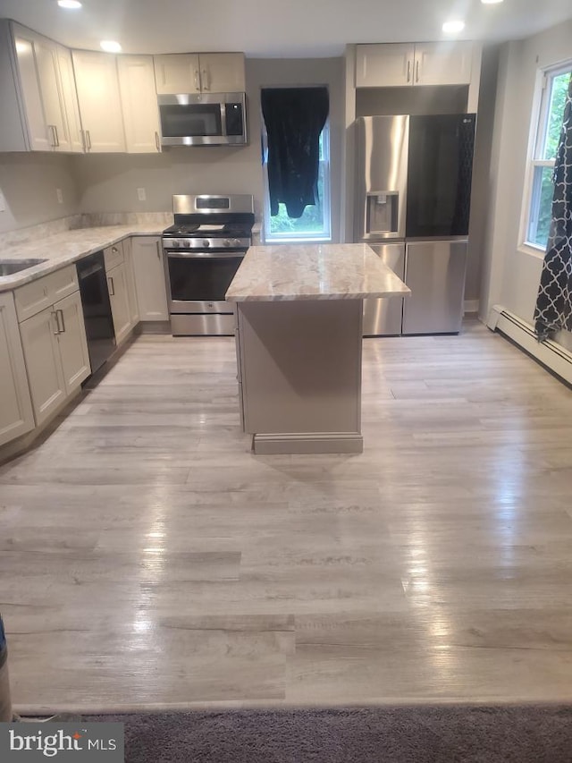 kitchen with appliances with stainless steel finishes, light wood-type flooring, a kitchen island, and light stone counters