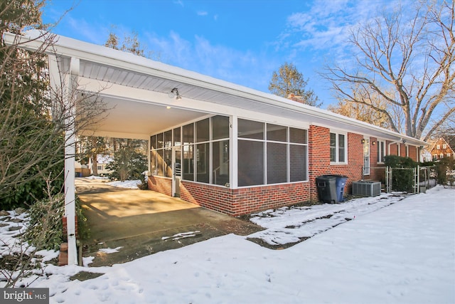 snow covered property featuring central air condition unit, a carport, and a sunroom