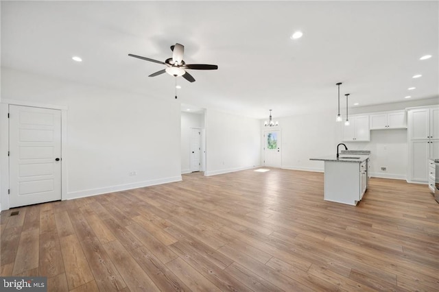 unfurnished living room featuring ceiling fan with notable chandelier, sink, and light hardwood / wood-style flooring