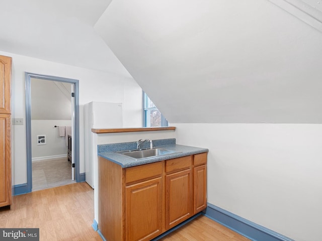 kitchen with sink, white fridge, light hardwood / wood-style floors, and vaulted ceiling