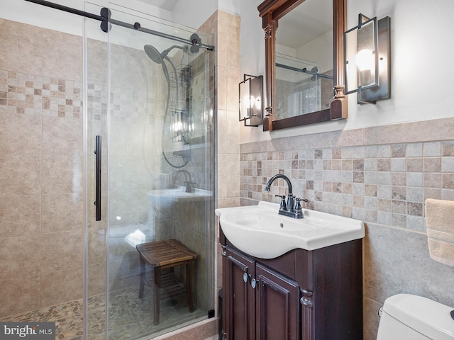 bathroom with vanity, a shower with shower door, tile walls, and toilet