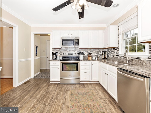 kitchen featuring sink, appliances with stainless steel finishes, white cabinetry, ornamental molding, and dark stone counters