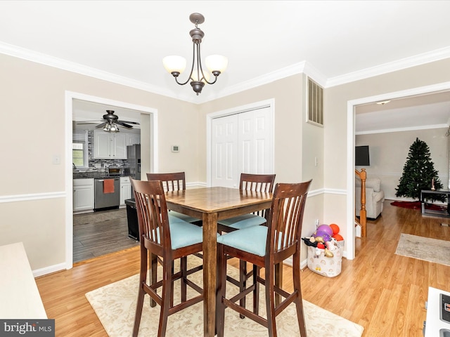 dining space with ceiling fan with notable chandelier, ornamental molding, and light hardwood / wood-style floors