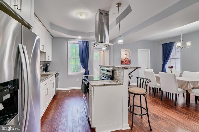 kitchen with pendant lighting, appliances with stainless steel finishes, white cabinetry, island exhaust hood, and light stone countertops