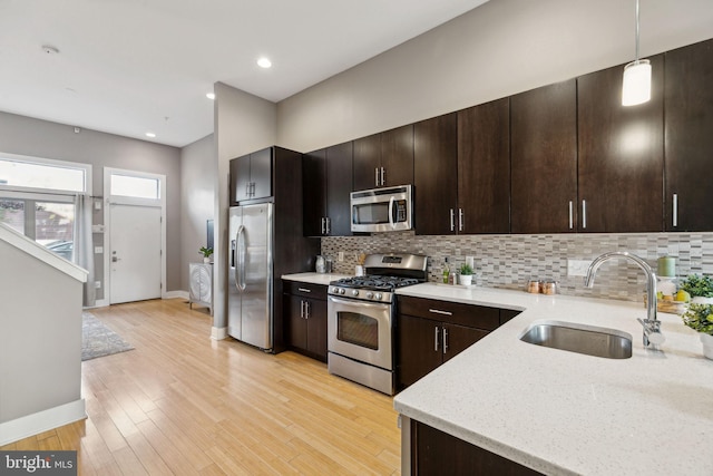 kitchen featuring light stone countertops, appliances with stainless steel finishes, sink, decorative light fixtures, and light hardwood / wood-style flooring