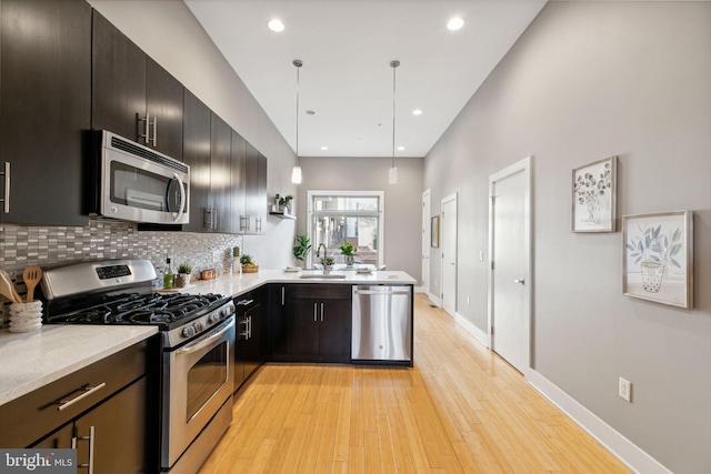 kitchen with sink, tasteful backsplash, light hardwood / wood-style floors, decorative light fixtures, and appliances with stainless steel finishes