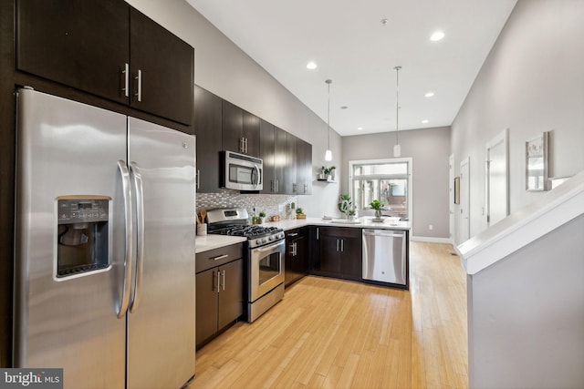 kitchen with backsplash, pendant lighting, dark brown cabinets, appliances with stainless steel finishes, and light wood-type flooring