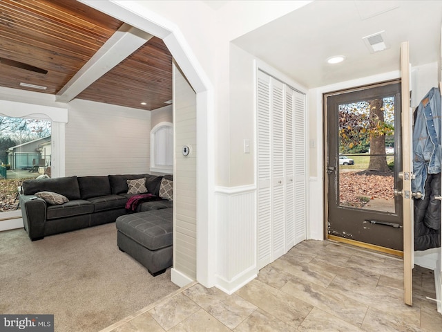 foyer featuring light carpet, beam ceiling, and wooden ceiling