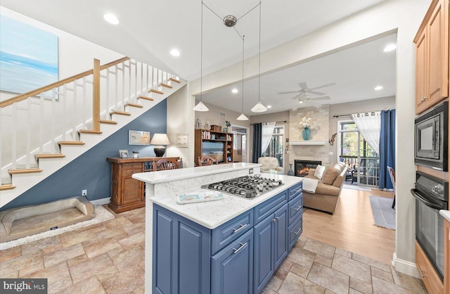 kitchen with pendant lighting, a center island, black appliances, blue cabinets, and a large fireplace