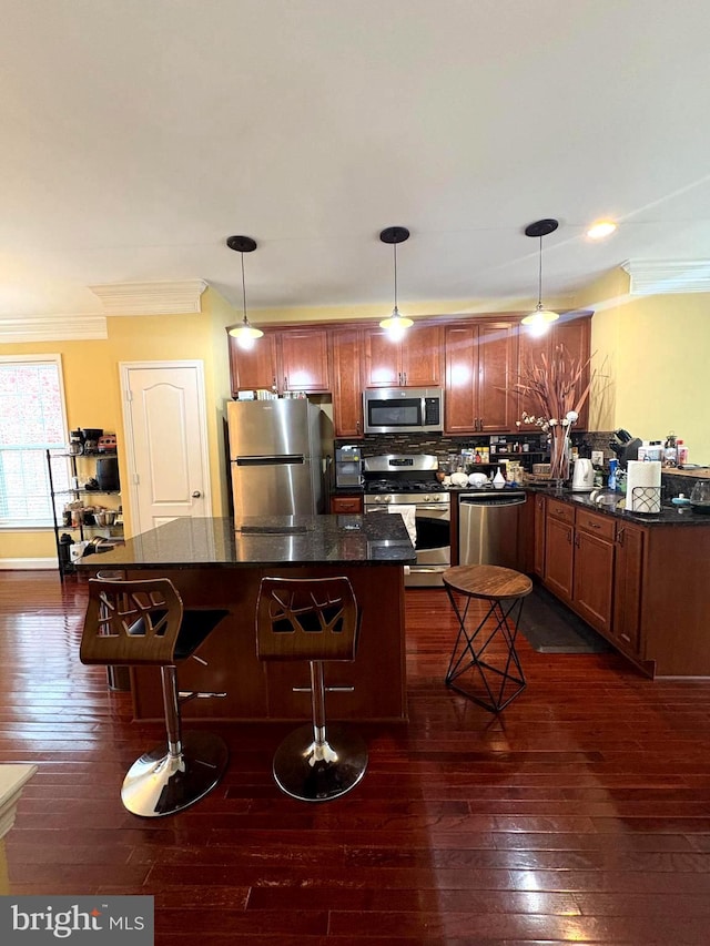 kitchen featuring a breakfast bar area, dark wood-type flooring, pendant lighting, and stainless steel appliances