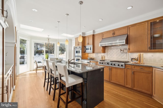 kitchen featuring decorative light fixtures, a kitchen bar, appliances with stainless steel finishes, ventilation hood, and light stone counters