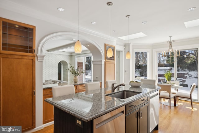 kitchen with a kitchen island with sink, dishwasher, hanging light fixtures, stone counters, and sink