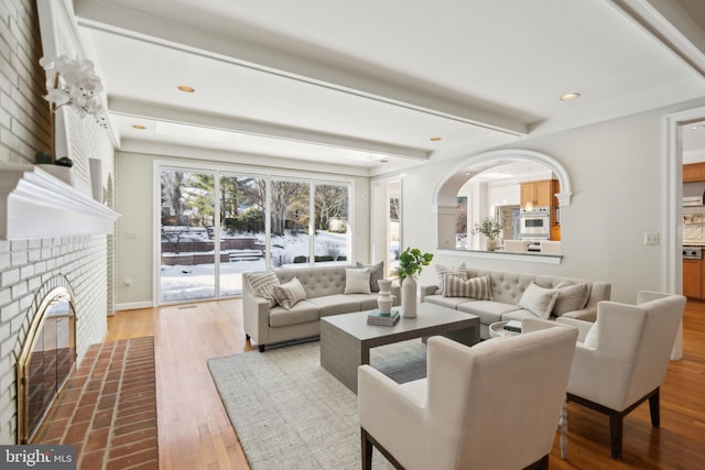 living room with beam ceiling, a brick fireplace, and hardwood / wood-style floors