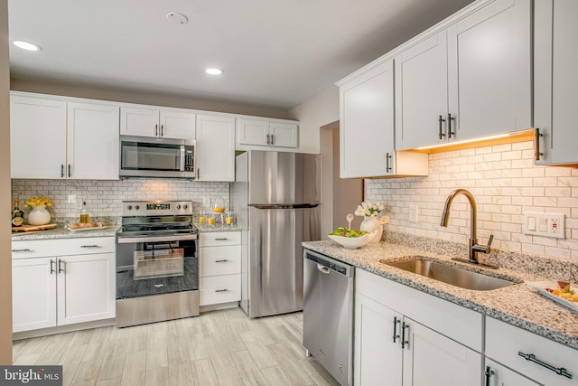 kitchen with sink, white cabinetry, stainless steel appliances, light stone counters, and decorative backsplash