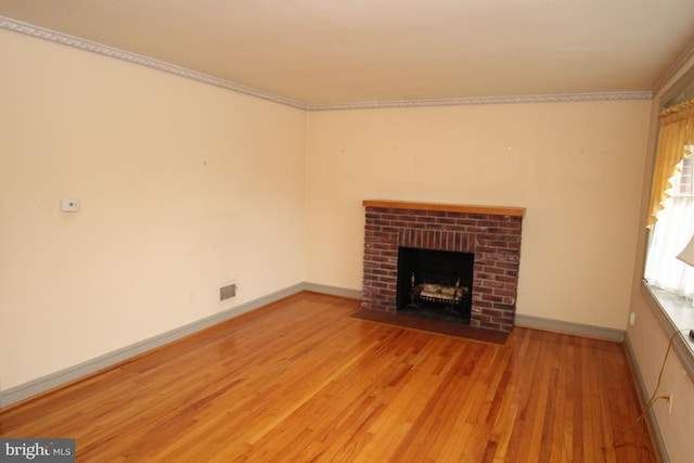 unfurnished living room featuring light wood-type flooring, ornamental molding, and a brick fireplace