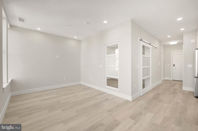 spare room featuring a barn door and light hardwood / wood-style floors