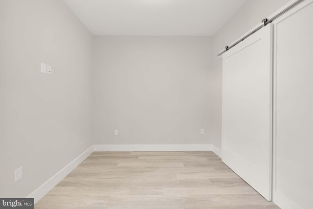 unfurnished bedroom featuring a barn door and light hardwood / wood-style flooring