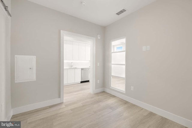 unfurnished room featuring sink, electric panel, and light hardwood / wood-style flooring