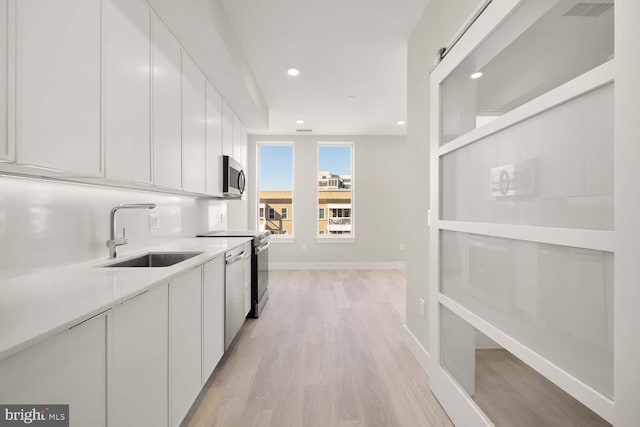 kitchen featuring white cabinetry, sink, light hardwood / wood-style floors, and appliances with stainless steel finishes