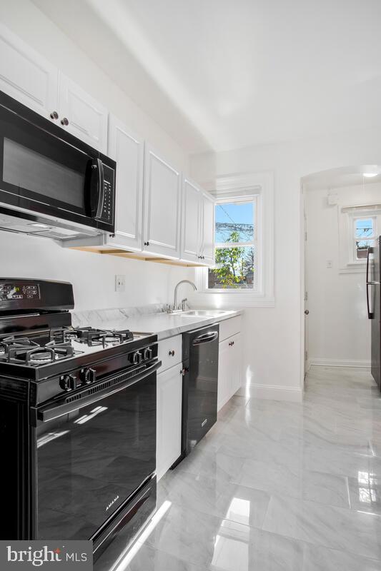 3917 Ridgewood Ave, Baltimore, MD 21215 - kitchen with black appliances, white cabinets, baseboards, a sink, and light countertops