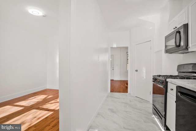 kitchen with light stone countertops, white cabinetry, black appliances, and light hardwood / wood-style floors