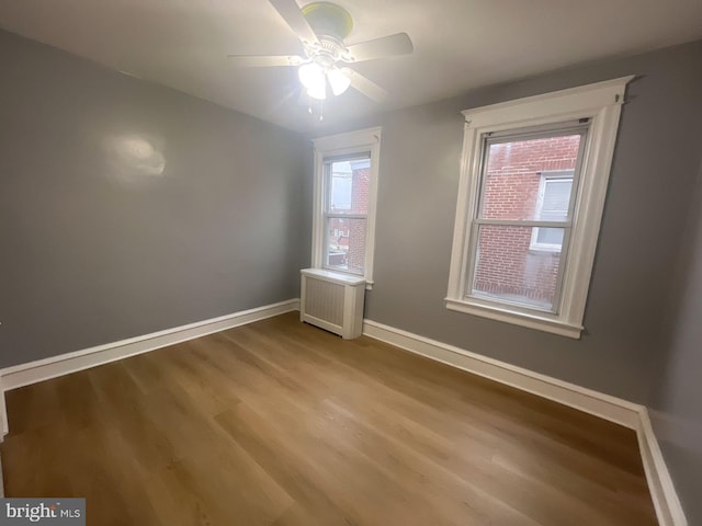 empty room with ceiling fan, plenty of natural light, light hardwood / wood-style floors, and radiator heating unit