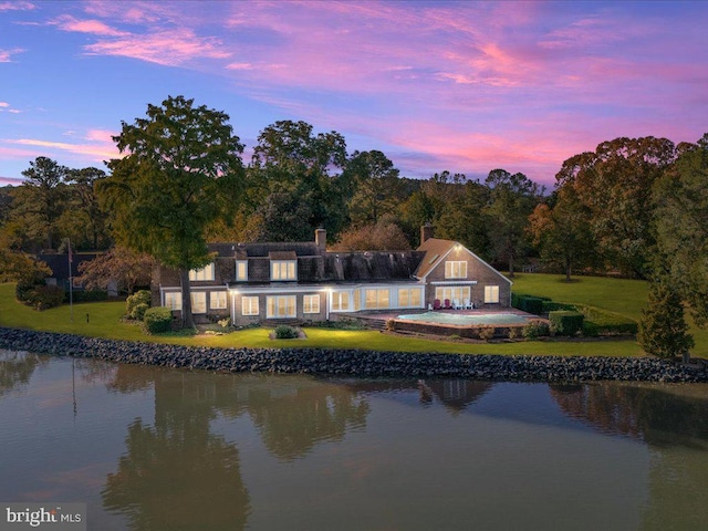 back house at dusk featuring a water view and a lawn