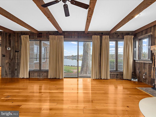 interior space featuring a healthy amount of sunlight, a water view, light hardwood / wood-style flooring, and wooden walls