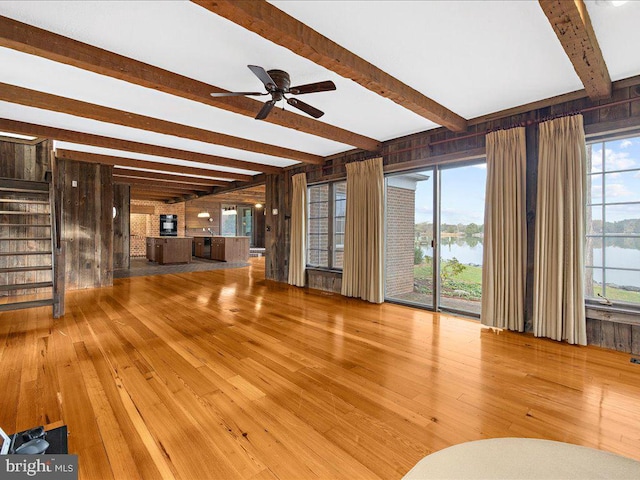 unfurnished living room featuring hardwood / wood-style floors, wood walls, a water view, and beamed ceiling