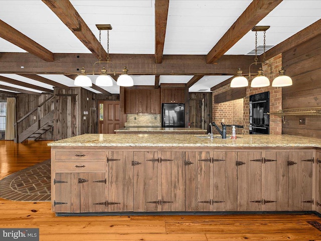 kitchen featuring black appliances, beam ceiling, hanging light fixtures, and wooden walls