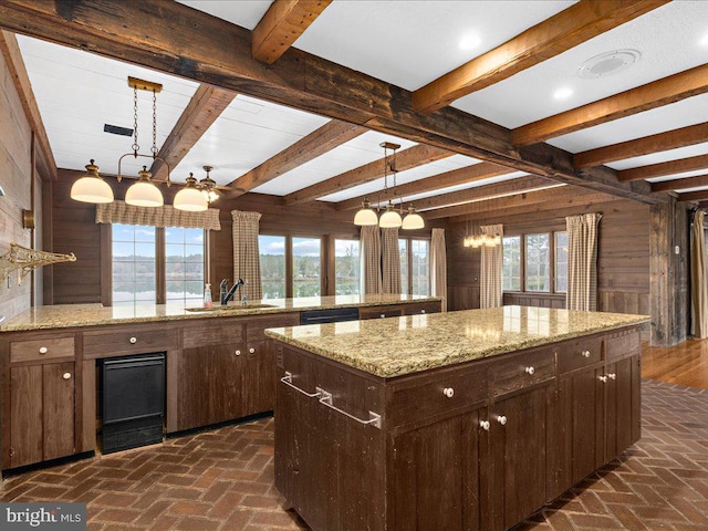 kitchen featuring sink, beam ceiling, hanging light fixtures, a large island, and wood walls