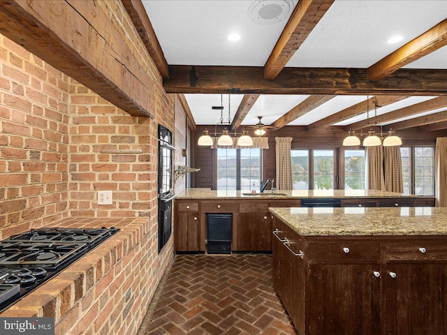 kitchen with sink, light stone counters, beamed ceiling, decorative light fixtures, and dark brown cabinets