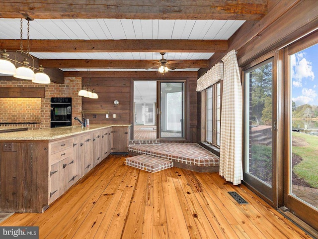 kitchen with hanging light fixtures, light hardwood / wood-style flooring, ceiling fan, light stone countertops, and beamed ceiling