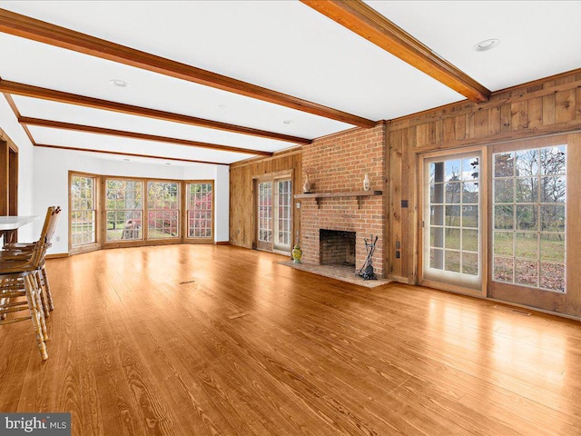 unfurnished living room with a wealth of natural light, beamed ceiling, light hardwood / wood-style floors, and a brick fireplace