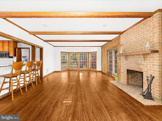 unfurnished living room with beam ceiling, a brick fireplace, and hardwood / wood-style flooring