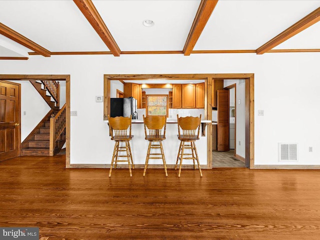 kitchen featuring beamed ceiling, black refrigerator, wood-type flooring, and a breakfast bar area