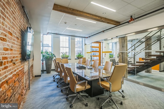 carpeted dining space featuring a drop ceiling and brick wall