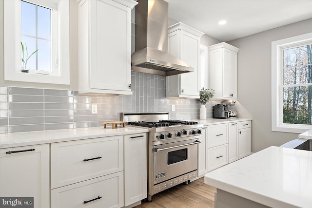 kitchen featuring premium range, white cabinets, wall chimney exhaust hood, decorative backsplash, and light wood-type flooring