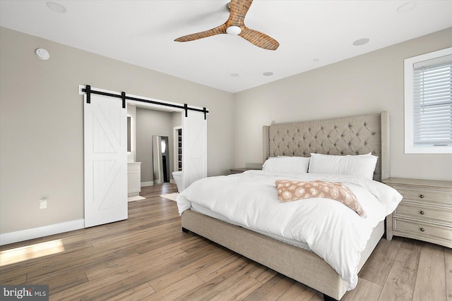 bedroom with a barn door, light hardwood / wood-style flooring, and ceiling fan