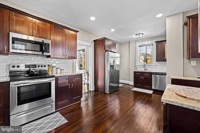 kitchen with sink, dark hardwood / wood-style floors, appliances with stainless steel finishes, tasteful backsplash, and light stone counters