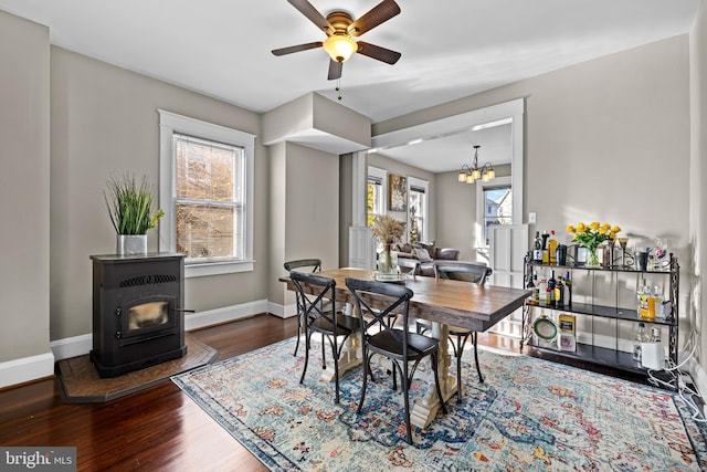 dining space featuring ceiling fan with notable chandelier, wood-type flooring, and a wood stove